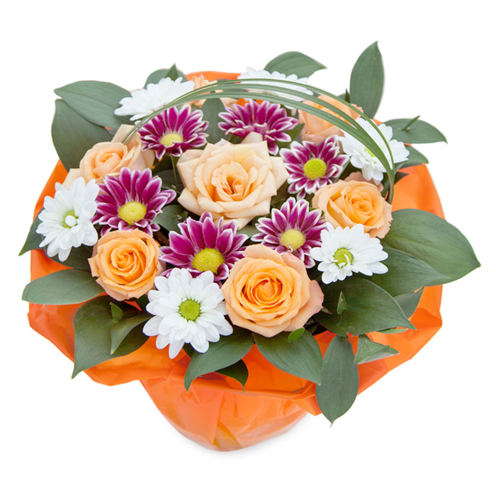 From a slightly elevated overhead view, this lively and lush bouquet radiates with the artistry and vibrancy characteristic of Oxford's finest florists. At the heart, plush peach-to-orange roses unfurl gracefully, their petals capturing warm, inviting tones that suggest a late afternoon stroll across University College quadrangles. Interspersed are groups of white chrysanthemums with dainty petals and green-yellow centers, providing a bright contrast reminiscent of the springtime blossoms in Florence Park. Deep magenta and purple chrysanthemums add a bold, sophisticated edge-each petal tight and vivid, rising from a cheerful lime center-recalling the vibrant displays at Oxford's Cowley Road flower shops. Encircling the blooms, thick green leaves serve as a verdant backdrop, their glossy surfaces reflecting the careful attention of a local florist attuned to freshness and structure. A slender, arched leaf of bear grass sweeps elegantly across the composition, introducing a contemporary, airy element like the spires that grace the city skyline. Wrapped securely at the base in bright orange cellophane, the bouquet is visually anchored and ready for gifting; the wrap's crinkled texture pick ups the warm hues of the flowers above, lending a cohesive sense of celebration. Crafted for occasions both joyful and heartfelt, this arrangement brings the unique allure of gardens and green spaces from around Oxford into homes and offices, ideal for thoughtful gifting, anniversaries, or simply to bring a splash of colour and optimism on a rainy day.