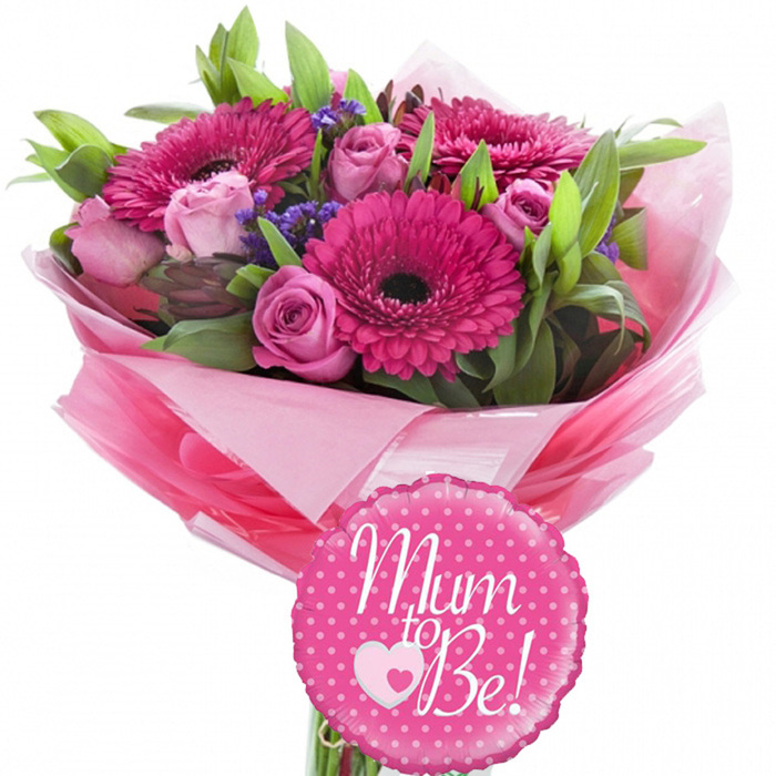 A hand-tied bouquet celebrating a mum-to-be is photographed against a pristine white backdrop, allowing every pink and green detail to stand out with clarity. Dominating the arrangement are several large fuchsia gerbera daisies, their broad, finely ribbed petals radiating in a circle around dark, almost chocolate-coloured centres, creating a strong focal point and a feeling of joyful energy. Interwoven with them are classic pink roses in a gentle, baby-soft hue, some just beginning to open with cupped petals, others forming tight buds that speak of moments yet to come. Between the main blooms, small clusters of purple filler flowers, likely statice or limonium, add a subtle mist of colour and a slightly wild, meadow-like texture that keeps the design from feeling too formal. The bouquet is framed with generous green foliage, from slim linear leaves that arch gracefully to fuller, glossy leaves that deepen the colour palette and lend the bouquet a fresh, garden-picked charm, as if it had been gathered from a cottage garden on the edge of Oxford. The stems are wrapped in layers of pink tissue paper in varying intensities, shaped into a soft, ruffled collar that flares around the blooms, then encased in a transparent, shiny cellophane sleeve that captures reflections like window light on Broad Street. Secured at the base, a small round foil balloon in bright pink with evenly spaced white polka dots provides a whimsical finishing touch. The balloon bears the message Mum to Be! in flowing white script, with a tiny pink heart nestled inside a white heart motif, symbolising both affection and the new life on the way. This harmonious combination of flowers and balloon feels perfectly suited to baby showers in Oxford, from cosy home gatherings to celebrations near the university colleges.