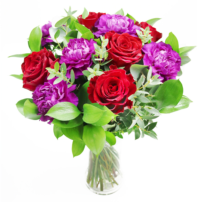 In this image, a refined bouquet of velvety red roses and lush purple peonies rises gracefully from a clear glass vase, the entire design poised somewhere between classic romance and modern Oxford chic. The roses, a deep, almost wine-red, open outward in layered spirals, each petal soft and slightly curled at the edges, suggesting both tenderness and passion. Nestled alongside them, the purple peonies are generous and full, their many ruffled petals overlapping to create spheres of texture that feel both opulent and inviting. The blooms are surrounded by an abundant halo of greenery: smooth, dark green leaves that fan out and slightly spill beyond the flowers, and slender strands of eucalyptus threading through the arrangement. The eucalyptus, with its soft, silvery-green leaves, introduces a hint of coolness, visually and aromatically, like stepping out from a bustling Oxford street into a quiet college garden. The stems are visible through the crystal-clear vase, submerged in water, carefully gathered but not rigidly tied, giving an impression of natural ease and freshness, as though the bouquet had just been arranged in a florist's studio off Cornmarket Street. Gentle natural light glances across the petals, highlighting their curves and shadows, making every rose and peony seem three-dimensional and alive. This arrangement would be perfectly at home on a dining table during an anniversary dinner in North Oxford, on a reception desk in an office near St Giles, or arriving as a same-day delivery to someone special anywhere in the city. It speaks of admiration, deep affection, and occasions worth remembering.