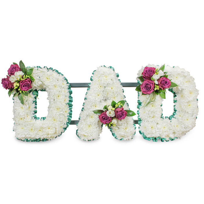 Artfully fashioned for a memorial, these three-dimensional letters spell DAD in bold capital form, each letter densely covered in pure white chrysanthemums that give the piece a plush, textured face. The chrysanthemums' tiny petals are closely set to create an unbroken field of white, the effect both serene and tactile. Each letter's silhouette is crisply defined by a ruffled emerald-green ribbon that follows every curve and angle, offering a respectful pop of colour and a traditional finishing touch. Small, emotional clusters of deep magenta roses are positioned with care - upper left of the first D, low in the A's central V, and upper right of the second D - and are offset by sprays of delicate white freesia and rich green foliage to add contrast, scent, and depth. A slim, dark-green or grey horizontal support behind the letters keeps the composition level for display on a service easel or at a graveside. As an experienced local florist in Oxford, we picture this arrangement set against the understated walls of a chapel near the High Street or placed by the graves of a family plot close to Botley Road; it speaks of steady love, quiet respect and personal farewell. Crafted with care and attention to texture, colour, and placement, this tribute from Flowers Oxford conveys a heartfelt, dignified message of remembrance for a beloved father.