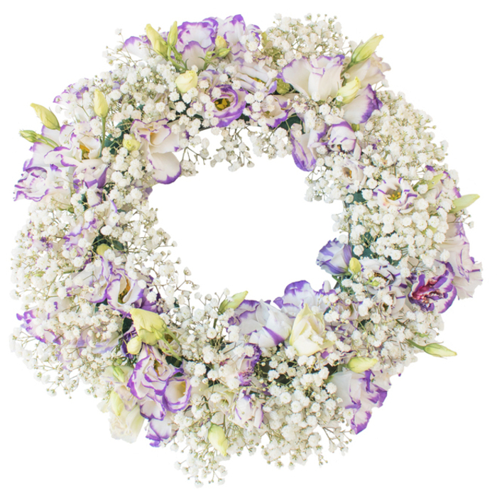 A lush circular funeral wreath fills the frame, carefully arranged against a bright white background so that the colours and textures of each bloom are clearly defined. The entire ring is thickly padded with Baby's Breath, the tiny white Gypsophila blossoms forming a dense, fluffy layer that brings to mind a soft cloud drifting above the dreaming spires of Oxford at dawn. Set at intervals within this snowy cushion are larger Lisianthus flowers, their ruffled petals creating subtle waves of movement around the wreath. These Lisianthus blooms are predominantly white, but each petal is finely traced and shaded with lavender and violet at the tips, resulting in a gentle, romantic contrast that feels both refined and understated. Some flowers open wide to reveal layered centres, while others are still unfurling from slender buds, showing hints of pale green and cream, which lend the design a sense of freshness and new beginnings. The wreath's inner circle is left clean and open, forming a neat halo of blossoms that would sit beautifully on an easel or rest flat at a funeral service in one of Oxford's chapels. There is no distraction from foliage or bold colours, just the quiet interplay of white and purple tones, emphasised by the neutral background. The overall impression is one of peace, purity, and tender remembrance, making this wreath a meaningful choice for commemorating a loved one, marking a memorial date, or offering condolences when words feel insufficient.