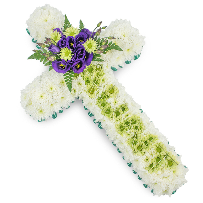 This image shows a carefully composed floral cross, crafted as a funeral or memorial tribute with a calm, contemporary elegance that would be at home in an Oxford church or crematorium chapel. The cross itself is fully covered with masses of white spray chrysanthemums, each small flower nestling closely to the next so that no gaps in the structure show through. The result is a plush, soft-looking surface that feels gentle and consoling, symbolic of peace and a life fondly remembered. Around the entire outline of the cross runs a slim border of vivid green, created either from ribbon or neatly folded foliage, which frames the white blooms and crisply defines the Christian shape, much like the green borders around paths in University Parks. Running down the centre of the long vertical arm is an elegant panel of lime-green button chrysanthemums, their tiny, rounded blooms forming a textured band of colour that contrasts beautifully with the surrounding white petals. Over this green inset, delicate pale green wires are draped in a subtle criss-cross or diamond pattern, adding a refined, almost embroidered detail. Where the vertical and horizontal arms meet, a small yet striking central spray draws attention: several deep purple lisianthus flowers, with ruffled, velvety petals and darker throats, are grouped together with bright lime-green chrysanthemums that echo the panel below. Soft fern fronds and glossy greenery fan out from behind this cluster, introducing movement and slight shadows. Created in the style of tributes prepared by Flowers Oxford for services across areas like Jericho, Iffley, or Marston, this floral cross balances tradition and modern design, offering a dignified, heartfelt expression of condolence in soothing shades of white, green, and purple.