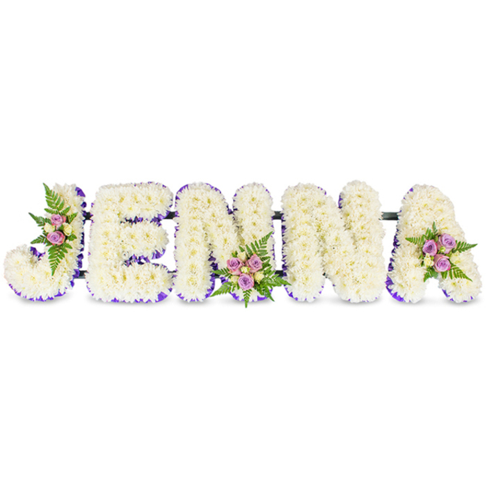 A meticulously arranged memorial piece spells JENNA in five bold, three-dimensional capitals, presented against an immaculate white surface that emphasises form and texture. Each letter is crafted from an abundance of small, creamy-white chrysanthemums - or comparable delicate florets - packed tightly to create a soft, cloud-like volume. A vivid deep-purple trim outlines the inner edge of each letter, either as a narrow ribbon or as a line of tiny purple blooms, which lends precision and visual depth to the otherwise monochrome field. The letters sit connected by discreet dark bars, a structural detail that stabilises the composition and allows it to be displayed prominently within a service space.

Three thoughtfully placed floral accents bring warmth and life to the tribute: the first on the upper left curve of the J, the second on the lower centre of the second N, and the third on the upper right curve of the A. These accents combine blush-pink and lavender spray roses with softer cream buds, set amongst delicate green fern fronds that add feathered texture and a fresh green scent. Under soft daylight - the familiar, gentle light found along Oxford's High Street or in chapels near University Parks - the arrangement feels both solemn and tender, a handcrafted sympathy tribute intended to give comfort and to personalise a farewell with beauty and reverence.