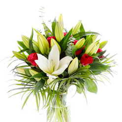 This composition reads like a small, graceful story of love and renewal: at its heart sits a single, open creamy-white Oriental lily, petals smooth and luminous, revealing pale yellow stamens and a soft green pistil that draw the eye. Surrounding that luminous centre are clusters of pale yellow-lime lily buds in varying stages of opening, suggesting movement and gentle anticipation. Interspersed among them are several rich, velvet-red rosebuds and small roses, their tight curls of petal offering sharp, romantic punctuation against the lily's calm hush. The greenery is abundant and textural-wide, deep forest-green leaves give the bouquet structure and visual depth, while arching, long-bladed palm fronds in a crisp emerald hue cascade outward to create rhythm and light-catching lines. Cool-toned eucalyptus stems with their round, silvery leaves soften the composition and introduce a subtle herbal note. The blooms and foliage sit in a clear, cylindrical glass vase, through which the pale green stems are visible in clean water, reinforcing the sense of freshness. Photographed against a plain white backdrop, the colours and textures are emphasized: the lily's creamy purity, the roses' theatrical red, and the layered greens. From an experienced florist's perspective, this arrangement suits celebrations across the city-from birthday tables near Jericho to elegant dinner parties by the Radcliffe Camera-and is ideal for anyone who wants a refined yet emotive gift that smells as inviting as it looks.