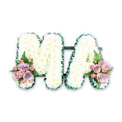 The image shows an elegant funeral flower tribute shaped into the letters MA, often chosen to honour a mother, mama, or a loved one whose initials are M.A. Set against a bright white backdrop, the design appears almost to float, allowing every detail of the craftsmanship to be appreciated. Each capital letter is densely covered in snowy white chrysanthemums, arranged so closely that not a gap of the base beneath can be seen. Their neat, button-like blooms create a plush, cushiony texture that feels soft and reassuring, reflecting purity and remembrance. A deep green border frames each letter, following the straight lines and angled points of the M and the graceful peak of the A. This contrast of white and green gives the tribute a refined, structured outline, much like the carefully maintained lawns and gardens around Oxford's colleges. At the base of the left upright of the M and the right upright of the A, small, thoughtfully placed sprays of roses provide gentle colour. Blush pink roses mingle with lavender-toned blooms and tiny pink spray roses, their spiral petals unfurling with quiet delicacy. Slender fern fronds and fresh foliage curl between the flowers, adding natural movement and a hint of countryside charm, reminiscent of walks along the Thames Path or through local parks. The overall effect is serene and heartfelt, a bespoke floral arrangement that would sit beautifully at a funeral service or memorial in Oxford, offering a personal farewell that combines traditional white sympathy flowers with soft pastel accents that speak of love, gratitude, and enduring connection.