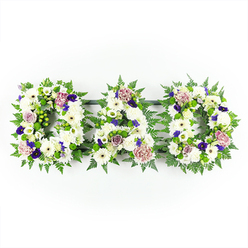 A serene and heartfelt funeral flower tribute spells out DAD in three separate floral letters, arranged side by side in a neat horizontal line against a spotless white background. Each capital letter is built from a dense carpet of fresh white chrysanthemums and white gerbera daisies, their rounded petals forming a soft, luminous surface that suggests purity, peace, and quiet reflection. Threaded between the white blooms are accents of pale mauve and lavender roses, along with softly ruffled lilac carnations, which add gentle pastel shading and emotional depth, like whispered stories shared about a father's life. Scattered more sparingly are touches of deeper purple flowers, resembling pansies or small spray chrysanthemums, their rich jewel tones bringing a sense of dignity and reverence that would feel at home in a thoughtful memorial service at one of Oxford's historic churches. The letters are edged and intertwined with lush greenery-delicate fern fronds and bright green foliage that outline the shapes clearly and add a fresh, natural contrast. The arrangement appears evenly lit, without harsh shadows, allowing the viewer to see every layered petal and the subtle interplay of green, white, and purple. This DAD floral tribute is both traditional and personal, ideal for families around Oxford who want to honour a beloved father with a custom floral display at a funeral, chapel of rest, or graveside. It conveys love, gratitude, and remembrance in a quiet yet unmistakably heartfelt way, much like the calm, reflective spaces found in the city's colleges and gardens.