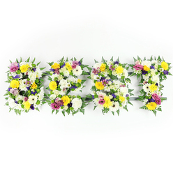 Presented against a clear, bright white backdrop, this horizontal tribute spells out BEST in four substantial floral letters, each one built from a tight mosaic of blooms and foliage that reads like a memory made manifest. The arrangement relies on a calming palette of crisp white chrysanthemums and cream gerberas, sunlit yellow roses and gerberas that seem to hold a warm afternoon glow, and small clusters of mauve to deep purple lisianthus which provide a gentle, reverent contrast. Vivid magenta-pink spray roses or carnations are woven through to offer small, joyful accents, while light-green and white filler flowers nestle into crevices to add softness and depth. Around each letter dark-green fern fronds fan out, creating a natural, almost lace-like border that frames the letters and tempers their solidity. Thin dark-green or metal support bars are discreetly visible where blooms cannot fully conceal the underlying structure, a sign of sturdy craftsmanship intended for display at a chapel, church hall, or funeral service. The head-on camera angle and evenly diffused lighting reveal petal textures, the faint leafy scent, and the fresh dampness of recently cut stems. As a florist's statement this piece balances bright, consoling colour with formal structure - an eloquent floral way to remember someone as the best, suitable for friends and family seeking an uplifting but dignified tribute.
