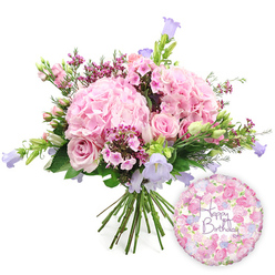 A luxurious birthday bouquet rests against a crisp white background, its colours echoing the soft pastels of blossom season along Oxford's riverside walks. The hand-tied arrangement is dominated by generous, rounded mounds of blush pink hydrangeas, their countless petals overlapping like delicate tissue, creating a pillowy, romantic texture. Nestled among these larger blooms are pale pink roses in varying stages of opening: some are fully unfurled with graceful, layered spirals, while others remain closed, promising a slow and beautiful reveal. Between them, tiny clusters of vivid fuchsia-pink waxflowers thread hints of deeper colour through the design, lending a fine, confetti-like detail that feels both playful and refined. Tall, bell-shaped campanula flowers in lavender and light purple rise lightly from the centre, their trumpet-like blooms curving upwards and outwards to add movement and height. The whole bouquet is wrapped in a frame of lush greenery, including slender, arching leaves and more solid, rounded foliage, which provides contrast and sets off the pastel tones. The stems are neatly aligned and visible at the base, suggesting a freshly prepared, garden-inspired bunch ready to be delivered across central Oxford, from Cowley Road to the quiet streets of North Oxford. Just to the lower right, a shiny round foil balloon catches the light, printed with a gentle floral pattern of small roses and buds in matching pinks and lilacs. Across its centre, in flowing purple script, the words "Happy Birthday" stand out clearly, turning this image into a complete snapshot of a joyful birthday surprise: flowers and balloon working together to send warm, heartfelt wishes.