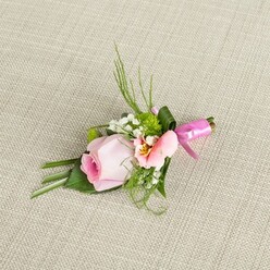 Resting gracefully on a textured, light ecru linen-a fabric reminiscent of the storied tables in historic Oxford libraries-this floral boutonniere captures the gentle elegance of a spring morning by the Cherwell. At the center, a tightly furled rose in pastel pink radiates an aura of serene anticipation, its core deepening to a richer pink before dissolving into the soft blush of its outer petals. Nestled alongside this central rose, an unfurling flower in lighter peach and pink shades opens to reveal buttery yellow touches and delicate, fine lines, reminiscent of Alstroemeria or Lisianthus blooms that might be found at Oxford's bustling covered market. Scattered throughout, tufts of pure white Baby's Breath evoke early morning mist over Port Meadow, while vibrant green cushion-like mums bring a playful, textural spark that enlivens the composition. Framing these blossoms, slender, spiky sprigs arch upwards like the elegant spires of the city, while broad, structured leaves are tucked and folded at the base to complete a harmonious whole. The stems are expertly wrapped with a gleaming, fuchsia pink satin ribbon, its small, artfully tied bow adding a festive splash of colour that suggests celebration and tradition. The soft daylight, diffused across the arrangement, bathes every element in warmth, highlighting shadow and sheen against the neutral, subtly woven background. Designed for special Oxford occasions-a college wedding, formal dinner, or graduation-this boutonniere marries romance, craftsmanship, and local spirit in every detail.