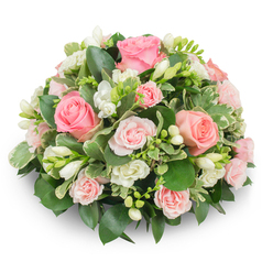 This bouquet brings to mind a still morning in an Oxford garden, tender and composed, with pale pink roses taking centre stage. The arrangement is compact and rounded, a cushion of flowers composed so closely that each bloom supports its neighbour: large, open roses display layered petals in soft blush and salmon tones, while clusters of smaller spray roses add delicate rhythm and scale. Interspersed throughout are elegant white freesias, some with bell-like blooms fully open and faint yellow stamens visible, others in slim buds promising gentle perfume later in the day. The foliage is abundant but refined - broad, glossy dark greens ground the composition, while variegated leaves with cream margins (reminiscent of pittosporum) lift the palette and introduce a light, almost silvered edge. The flowers are set against a stark white background and arranged so no stems show, giving a formal, polished silhouette that still reads as natural and comforting. Light is soft and diffuse, catching the textures of velvety rose petals and the translucent frills of freesia, enhancing a sense of quiet grace. Suitable for a sympathy tribute, a dignified funeral display, or as a gentle anniversary gift, this piece would feel at home in a sitting room near the Covered Market or as a simple memorial on a table at a small service in Summertown, where understated beauty and heartfelt sentiment are valued.