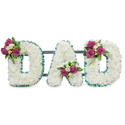 This solemn floral composition presents the word "DAD" in large, sculpted letters, each letter formed from hundreds of small, snow-white chrysanthemums that create a continuous, cloud-like surface. The tiny, densely packed blooms lend a soft tactile richness, the petals layering into gentle undulations that diffuse light and suggest purity and peace. A narrow, folded emerald-green ribbon traces the outer and inner edges of every letter, its pleated texture providing a cool, composed contrast to the warm, round shapes of the chrysanthemums. Each letter bears a carefully placed accent of saturated magenta roses, their scent faintly sweet against the quiet backdrop of white; these clusters are complemented by sprays of white freesia and slender, glossy foliage, which add sparkle and sculptural definition. The first D holds its bouquet high on the left curve, the A's cluster nestles into the lower V, and the final D mirrors the first with a bloom cluster on its right curve - a balanced, intentional choreography of color. A discreet dark-green or slate support bar runs behind the letters, suggesting the arrangement is designed for standing display at a chapel, crematorium, or graveside. Imagined in soft morning light, this tribute evokes restrained elegance and familial steadiness - a fitting floral farewell for a father, available from local florists serving Oxford and nearby Summertown or Headington.