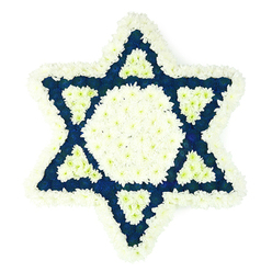 A striking Star of David floral tribute fills the frame, its precise geometry picked out in fresh white and deep blue flowers against a plain, bright white background. The entire six-pointed Magen David is edged with a soft, cushion-like border of white chrysanthemums or similar multi-petalled blooms, giving the outer shape a gentle, feathery texture while still holding a clean, defined outline. At the centre sits a bold white hexagon, perfectly formed from closely packed blossoms that seem almost quilted in texture, like a still, peaceful core. Surrounding it, the six triangular points of the star are richly filled with dark blue or indigo flowers, their saturated colour recalling the deep blues seen in traditional tallitot or synagogue fabrics in areas like Summertown, Cowley, and central Oxford. Nestled within the base of each blue point is a smaller triangle of white blooms, creating a delicate interplay of colour and form that suggests interwoven lives and shared heritage. The design is flat yet full-bodied, with layers of petals giving depth and dimension to the otherwise two-dimensional star. There are no vases, ribbons, or extra foliage-just the powerful Jewish symbol rendered purely in flowers, designed for placement on an easel or as a casket-side tribute at a funeral or memorial service. The overall impression is one of reverence and quiet strength, an expertly crafted sympathy arrangement that could be chosen by families in Oxford seeking a meaningful Jewish funeral flower piece to express love, respect, and remembrance.