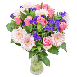Every nuance of this radiant bouquet reflects the care and craft of an Oxford florist attuned to the rhythms of local gardens and winding streets. The composition glows with luminosity: soft pink gerberas and classic roses blend with watercolor subtlety, their pastel tones echoing the first pink light over Magdalen Tower. Spires of deep purple statice punctuate the bouquet, adding pops of vibrancy that evoke the lively bustle of the Covered Market in spring. Fresh, dewy foliage grounds the arrangement, its green veins cool to the touch, providing a rich foundation reminiscent of the leafy paths along Christ Church Meadow. The translucent glass vase refracts gentle sunlight, offering an invitation to draw closer-whether as a cheerful gesture for a friend recovering in Summertown, a thoughtful centerpiece for a High Street home, or a joyful accent brightening a lively Oxford gathering. Every detail speaks of joy, optimism, and an unwavering attention to the harmony of colour, texture, and mood, making the arrangement as much a part of Oxford as its dreaming spires.