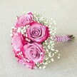 A striking bridal bouquet, artfully assembled by Flowers Oxford, rests atop a light, linen-textured surface reminiscent of the city's historic charm. The arrangement features about five vibrant roses, their petals resplendent in a seamless blend-from cool lavender and gentle mauve at their hearts to bold, fuchsia pink along the ruffled edges-capturing the eye with dynamic colour transitions and fluid depth. Interspersed among these blooms are soft clouds of white baby's breath, infusing the bouquet with airiness and refinement. The bouquet's stems are tightly bound and enveloped in a luxurious deep plum satin ribbon, finished with graceful swirls of lustrous white pearls-an elegant touch that echoes Oxford's rich traditions. Exposed green-brown stems lend a natural accent beneath the opulent wrapping. Bathed in soft, natural light and surrounded by Oxford's storied ambience, this bouquet is ready to complement a wedding at St John's College, a cherished anniversary, or any joyful Oxford occasion. The arrangement reflects the florist's attention to detail, bringing together classic romance and local character in every petal and pearl.