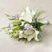 Lying across a softly textured, off-white linen backdrop that could grace a college hall in Oxford, this lush bouquet is a true testament to the area's blend of heritage and natural beauty. Majestic white lilies with wide, recurved petals command the heart of the arrangement, their pure hue complemented by subtle honey-yellow anthers and gentle brown speckles. Interspersed among these are clusters of lisianthus blooms, petals papery and white but edged in a dramatic purple that brings in the vibrancy of Magdalen College gardens. Adding a sense of vertical lift, slender stems of deep purple Veronica rise among the softer blooms, while delicate white baby's breath threads through for a misty, romantic air. The bouquet overflows with textured greenery-broad, deep green leaves form a solid base, while sprays of light, feathery asparagus fern arch outwards, recalling Oxford's riversides in spring. The stems are neatly aligned, bound in a satin white ribbon for a chic, bridal finish. Caught in gentle light, this bouquet glows with freshness and optimism, perfect as a wedding bouquet, anniversary surprise, or elegant centerpiece for celebrations across Oxford. Every blossom and leaf is selected with care by Oxford's seasoned florists, evoking serenity, purity, and enduring love.