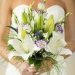 Wrapped in the poetic stillness of Oxford mornings, this bridal bouquet embodies the quiet anticipation of a new chapter. White Oriental lilies, open and resplendent, offer their freckled faces and golden stamens as a centerpiece, their soft fragrance mingling with memories of leisurely walks along the Isis. Nearby, ruffled white lisianthus edged with a trace of lavender reveal both spirit and whimsy-mirroring the magical nooks of Oxford's university quads in early spring. Dramatic spikes of royal purple Veronica stand tall among airy, white gypsophila, whose delicate, cloud-like clusters evoke the timeless romance woven into Oxford's winding lanes. Artful foliage-a lush tapestry of deep greens, unopened buds, and wispy ferns-cascades around the blossoms, giving the arrangement a sense of movement and freshness as if caught by a gentle Thames breeze. The bouquet rests lightly in the bride's hands, fingers elegantly polished, creating a subtle interplay between human touch and natural artistry. Every detail, from the harmonious blend of colours to the soft, luminous backdrop, is a testament to Flowers Oxford's devotion to craft, making this arrangement the perfect companion for a wedding celebration in one of the world's most storied cities.