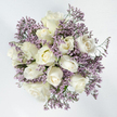 Captured from a bird's-eye view, this bouquet creates a soothing circle of white and lavender, perfectly centred on a bright, uncluttered white background. Around a dozen white roses are nestled together so closely that their rounded forms almost touch, creating a smooth, continuous ring of blooms. The roses are at varying stages of bloom: some are still modest, bowl-shaped buds, while others are beginning to unfold, their petals loosening into soft spirals, and a few are fully open, showcasing their intricate, layered hearts. Their colour is predominantly a cool, clean white, with subtle undertones of ivory and pale cream where light and shadow meet deep inside each flower. Surrounding and threading through these roses is an airy layer of lavender limonium, its countless tiny blossoms forming a gentle purple haze. The limonium's fine, branching stems and papery flowers contrast beautifully with the lush, velvety texture of the roses, adding volume and a sense of movement, almost like a soft cloud drifting around the central blooms. Only slivers of green foliage are visible, quietly supporting the structure from beneath. To me, as an Oxford florist, this is the kind of arrangement that might be delivered to a quiet terrace home near Iffley Road or placed in a reflective space overlooking the dreaming spires, offering comfort without any need for words. The overall mood is peaceful, graceful, and contemplative - a refined sympathy bouquet that conveys solace, remembrance, and heartfelt care through its gentle interplay of white and lavender tones.
