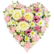 A beautifully detailed, heart-shaped funeral tribute fills the frame, standing out clearly against a spotless white background, as if ready to be carried into a quiet Oxford chapel or laid near a graveside overlooking the countryside. The florist has packed the heart densely with fresh flowers so that it appears rich and full, a tapestry of gentle colour and texture. At the centre, several full, creamy yellow roses open in graceful spirals, their velvety petals catching the light and suggesting warmth, comfort, and lasting devotion. These central roses are held within a generous bed of pale pink carnations, whose soft, feathery petals overlap in ruffled layers, shaping the outline and main body of the heart and creating a sense of embrace. Bright white spider chrysanthemums punctuate the design, each one composed of many slender, spiking petals surrounding light green centres, bringing a crisp contrast and a touch of airiness to the otherwise plush surface. Scattered among them, deeper magenta-pink lisianthus blooms add a note of intensity and emotional depth, their slightly frilled, bell-like petals drawing the eye. Small sprigs of green foliage peek from between the flowers, adding natural freshness that calls to mind the gardens and college quadrangles across Oxford. At the very tip of the heart, a narrow pink ribbon is just visible, suggesting this piece has been lovingly prepared as a sympathy or memorial arrangement. The finished design feels both tender and dignified, an expression of enduring love and respectful farewell that would offer solace to family and friends gathering to remember someone dear.