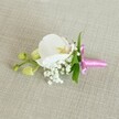 A delicate white orchid boutonniere lies horizontally on a soft, oat-coloured linen background, the neutral fabric gently textured like a favourite summer jacket, allowing every floral detail to stand out. At the heart of the design is a single Phalaenopsis orchid bloom, its broad, velvety petals a pristine, luminous white that curves softly outward. At the centre of the flower, the throat glows with fine touches of pale yellow and the faintest blush of pink, giving the orchid a quietly romantic character. Tucked closely around its base, tiny tufts of white baby's breath cluster like little clouds, their hundreds of minuscule blossoms adding a misty, ethereal halo. A few slender, bright green leaves peek from behind the bloom, offering a crisp, fresh contrast to the creamy petals and soft background. To one side, a short stem extends, tipped with several tightly closed, lime-green orchid buds that suggest new life and the promise of blooms to come, as if poised to open just in time for the ceremony. The stems are neatly gathered and wrapped in a bright fuchsia satin ribbon, tied into a small, tidy bow whose glossy sheen catches the light and adds a joyful, celebratory note. The gentle, even lighting in the image emphasises the smoothness of the orchid, the airy texture of the Gypsophila, and the weave of the linen beneath. The overall mood feels serene and refined, perfect for a groom or prom guest walking through Oxford's historic streets after a ceremony near the colleges or along the High Street, carrying a quiet sense of elegance and care.