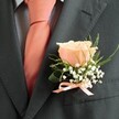 Embodying understated elegance, this classic boutonniere blends the romance of a peach blush rose with the anticipation of a wedding day in Oxford-possibly steps from the gentle bustle of Summertown or within a grand ceremony hall. The central bloom releases its soft petals in a swirl of buttery peach, capturing shafts of light like those that play across the Radcliffe Camera at golden hour. Baby's breath clusters around the rose, frothing delicately to evoke the gentle haze of morning dew over Oxford lawns. Subtle touches of green foliage-maybe inspired by foliage from local parks and riversides-arc upward in a lively, fresh display. The floral arrangement is nestled neatly against a sharply cut, charcoal-grey suit, while a peach satin ribbon at the base ties the entire composition together and mirrors the carefully chosen necktie, offering balance and polish. Light as a sigh, the boutonniere's fragrance hints at a summer orchard, only present to those who lean close. Expertly crafted by a florist who knows Oxford's celebrations and traditions, this buttonhole is more than a detail-it is a token of joy and unity created for cherished memories beneath dreaming spires.