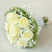 As a florist in Oxford I often assemble bridal pieces that feel both classic and modern; here, seven prominent creamy-white roses form the heart of the bouquet, each bloom opening in soft, layered spirals that suggest warmth and tenderness. Interspersed among them are delicate clusters of pure white gypsophila, which float like mist and give the arrangement an ethereal, cloudlike dimension. Graceful loops of green bear grass are threaded around the outer edge, framing the roses and adding a crisp, verdant contrast that evokes strolls through the Botanic Garden. The stems are bound securely into a comfortable handle and wrapped with a lustrous silvery-white satin ribbon, finished with multiple rows of tiny, iridescent pearl beads-an elegant, tactile detail that catches natural light and invites touch. The bouquet lies at a diagonal on a neutral beige textured fabric, lending a warm background that highlights the creamy tones and delicate sculptural shapes. Lighting is soft and even, chosen to reveal petal texture and the fresh sheen on the foliage without overpowering the composition. You can almost sense the faint sweet perfume of the roses and the faint green note from the bear grass. This design, crafted by Flowers Oxford for brides and special occasions across Jericho, Summertown, and the city centre, reads as timeless romance-equally suited for a riverside vow at the Cherwell or a small college celebration-and available for careful local delivery when same-day freshness matters.