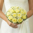Soft butter-yellow roses take centre stage in this hand-tied bridal bouquet, each bloom opened to show concentric spirals of velvety petals that glow with a faint, warm luminosity. Interspersed among them are clouds of tiny white baby's breath, their delicate, frothy texture lifting the composition and creating points of visual air that feel like soft exhalations. Around the perimeter, looping strands of glossy green grass form a subtle, architectural rim, curving inward to cradle the roses and add a clean, modern counterpoint to the vintage softness of the petals. When carried by a bride in classic lace, the bouquet reads as quietly elegant - hopeful and restrained, suited to an intimate ceremony by the Radcliffe Camera or a small reception near the Covered Market. The scent is gentle and evocative: a pale honey note from the roses threaded through fresh green hints from the foliage, not overpowering but present enough to be noticed in close moments. As a local florist preparing bouquets at Flowers Oxford, I choose materials and shaping that photograph well and feel natural in hand, mindful of light, scale, and the pace of a wedding day here in Oxford. The arrangement's sober palette and compact dome make it versatile - equally appropriate for a civil service in Jericho or a chapel ceremony on High Street - and its craftsmanship speaks to an intention to make the bride feel calm, held, and quietly celebrated.