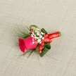 A richly detailed boutonniere is laid on a softly textured, light beige linen background, its natural fibres catching the gentle daylight like the woven cloths seen on market stalls in Oxford's Covered Market. At the centre, a single deep fuchsia rose forms the heart of the design, its velvety petals tightly layered and just beginning to unfurl, suggesting a moment of romance about to blossom. Around the rose, frothy clusters of tiny white baby's breath add a cloud-like softness, their delicate blooms creating a gentle contrast against the bold pink. Nestled between the white flowers, glossy red hypericum berries gleam like polished beads, bringing a festive brightness and a touch of rustic charm that feels perfectly at home in a historic city wedding near the Bodleian or along St Giles. Wisps of fine, fern-like greenery extend from the base, airy and light, while broader dark green leaves are carefully curled and shaped to frame the central rose, giving the small piece a sense of structure and depth. The stems are wrapped neatly in a rich red satin ribbon, tied with precision into a small, tidy bow that echoes the warm tones of the berries and the rose. Seen from a gently elevated angle, every curve of the petals, every sprig of foliage, and every gleam on the berries is visible, showcasing the florist's craftsmanship. The overall mood is one of elegant celebration, ideal for a groom or groomsman at an Oxford wedding, or for any formal event where a simple lapel is transformed into a quietly luxurious statement of joy and affection.