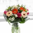 This bouquet, crafted by a local Oxford florist, bursts forth as a radiant celebration of colour and texture-a vivid composition that delights both the eye and spirit. At its heart, creamy peach gerbera daisies fan out in soft, welcoming rays, evoking the warmth of first light tracing across Magdalen Bridge. Bright orange gerberas punctuate the assembly, their spirited tones adding an exuberant energy. Vivid magenta roses, their velvety spirals unfolding with romantic flair, nestle gracefully amongst the lighter blooms. Ivory alstroemeria and petite white flowers peep through layers of lush green foliage, their gentle fragrance conjuring serene Oxford mornings near Christchurch Meadow. Broad, glossy aspidistra leaves cradle the arrangement, providing a supportive, structured frame reminiscent of the city's protective college cloisters. The clear glass vase allows refreshing green stems to show through, heightening the bouquet's organic, newly-gathered charm. Illuminated by cool, natural light, each hue glows with vitality, suggesting joyous occasions-whether brightening a room in Jericho, celebrating with friends at a local café, or expressing heartfelt thanks across the city. Every detail of this bouquet speaks to the artistry and dedication of Oxford's floral tradition, making it a meaningful gesture of appreciation or congratulations.