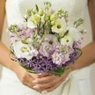 Like the quiet elegance of Oxford's cloisters, this bridal bouquet is a vision of romance and gentle sophistication. Creamy white Lisianthus-fully open with delicately ruffled petals and subtle green-yellow centers-anchor the arrangement, symbolizing purity and tender affection. Pale green Lisianthus buds and sprays of soft lilac and blush-pink stock nestle closely together, filling each pocket of the bouquet with fragrance and a hint of joyous anticipation. Contrasting these whisper-light blooms is a distinctive band of vivid purple Allium stars at the bouquet's base, providing dramatic visual interest as if echoing the bold silhouette of Oxford's spires at twilight. Loops of sleek bear grass, deep and glossy, encircle the arrangement in carefully considered arcs, adding both structure and a touch of contemporary flair. The bride's hands, neatly manicured in a demure pastel shade, cradle the stems with care. In the gentle blur behind, the pale shimmer of a wedding dress is just visible, blending seamlessly with the bouquet's serene palette. Crafted with artistry honed in Oxford local workshops, this bouquet radiates freshness and dreamy charm-an ideal accompaniment for weddings at Magdalen College gardens, by the Cherwell, or in the heart of the city's historic quarters-inviting the senses to linger amid the soft scents and silken petals.
