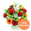The photograph presents a joyful, celebratory bouquet designed in a clear rectangular glass vase, styled in a way that feels perfectly suited to an Oxford home, whether near the Bodleian or along leafy Cowley Road. Around the base of the vase, a soft light green and white gingham ribbon is neatly wrapped, adding an inviting, homely character. Rising above, the flowers form a compact, dome-like arrangement brimming with colour. Deep red roses, their petals velvety and tightly layered, nestle beside red-orange carnations whose frilled, multi-petalled heads add a sense of abundance. Bright orange gerbera daisies, each with a prominent dark centre, fan outwards like small suns, creating a lively rhythm across the bouquet. White Oriental lilies provide height and elegance, some blooms fully open to reveal subtle pink stripes along the inner petals and pollen-dusted stamens, while others remain closed in smooth, tapering buds, suggesting longevity and freshness. Threaded between these focal flowers are clusters of lime green pompom chrysanthemums, their small, round heads adding a fresh, zesty contrast that enlivens the whole design. Surrounding and supporting the blooms, deep green leaves and softly rounded sprigs of silver-green eucalyptus extend just beyond the main cluster, lending a natural, airy outline. The stems are clearly visible through the water-filled vase, cleanly cut and orderly. In the lower right-hand corner of the image, a circular orange badge overlays the scene, with bold white capital letters reading VASE INCLUDED, making it clear that the arrangement arrives complete, just as shown-an ideal choice for same-day flower delivery around Oxford for birthdays, thank you gestures, or simply brightening a quiet study or sitting room.