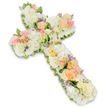 A large and reverent floral cross dominates the scene, resting against a pristine white background that mirrors the calm atmosphere of a quiet chapel in Oxford on a still morning. The cross is formed entirely from fresh flowers, arranged so thickly that the base is completely hidden under a soft, continuous layer of petals. The overall palette is tranquil and inviting: creamy whites and ivories provide the main structure, while gentle touches of pale pink, peach, and apricot roses add warmth and human tenderness. Full, velvety roses and smaller rosebuds are carefully grouped along the length of the cross, drawing the viewer's eye from the top down to the base and outward along each arm. These focal blooms sit atop a generously packed foundation of white hydrangeas and petite white roses or similar blossoms, whose rounded clusters create a plush, cloud-like texture across the entire shape. This density of flowers softens every line so the Christian cross appears welcoming and lovingly crafted rather than stark. Scattered sparingly among the petals are tiny specks of lavender or soft purple filler flowers, adding intricate detail and a gentle, cool-toned accent without disturbing the pastel harmony. Delicate glimmers of fresh green foliage show at the edges and between blooms, giving the cross definition, depth, and a natural garden-like freshness. The lighting is bright yet gentle, with a faint shadow beneath the arrangement that lifts it slightly from the background and emphasizes its three-dimensional form. Designed as a sympathy or funeral tribute, this floral cross serves as a moving expression of faith, peace, and remembrance, offering families in Oxford a tender way to honour a loved one's life and legacy.