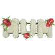 A tender, three-dimensional floral tribute carefully shaped to spell the word 'MUM' in bold capital letters, presented against a quiet white background. Each letter is formed from hundreds of small, pristine white spray chrysanthemums, their tight, rounded petals packed so densely the surface reads like a cloud of soft, matte ivory. The chrysanthemums create a cushiony, almost velvety texture that suggests quiet comfort when seen up close. A subtle dark green structural frame peeks out along the edges of the letters, giving the piece clean lines and a steady weight while remaining visually unobtrusive. Across this pale canvas, three glossy red anthuriums punctuate the composition - each with its characteristic heart-shaped spathe and a pale white-yellow spadix - providing a warm, poignant contrast to the white blooms. One anthurium sits on the upper left curve of the first 'M', another nestles gently at the base of the 'U', and the third crowns the upper right curve of the final 'M'. Clusters of feathery fern fronds and broader dark green leaves cradle each red bloom, while thin, arching blades of grass or long green stems sweep between the flowers, visually linking the letters with a flowing, organic line. Under soft daylight the arrangement reads as both crisp and comforting; the chrysanthemums breathe purity and the anthuriums offer a quiet, passionate note of remembrance. This classic sympathy piece is hand-finished with the careful technique of a seasoned florist and is ideally suited for a funeral service, wake, or graveside tribute to a much-loved mother, conveying respect, love, and enduring memory.