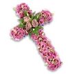This image shows a deeply expressive floral cross, placed against a pure white background where a faint drop shadow hints at its depth and dimensionality. The entire cross is cloaked in fresh flowers, giving it a soft, abundant appearance that feels both comforting and quietly dignified. Along the length of the vertical stem and across the horizontal arms, countless lisianthus blooms in shades of soft pink, mauve, and light purple are woven together. Their ruffled petals create a rippling, fabric-like surface, with some blooms displaying richer pink tones and darker centres, adding depth much like the layered colours of Oxford's Botanic Garden borders in late spring. At the very centre of the cross, where the arms meet, three roses serve as the heart of the tribute. Fully open and luxuriously petalled, they sit in tones of muted dusty rose and gentle mauve, gently cupped by fresh greenery. Fern fronds and small, bright green leaves frame these central blooms, bringing a vivid contrast that lifts the pastel tones. Between the larger flowers, small accent blossoms in pale pink, lavender, and creamy white, along with tiny green buds, provide intricate detail and a sense of careful craftsmanship. Along the contour of the cross, glimpses of darker purple ribbon or supportive material peek discreetly through, outlining its sacred form. This arrangement feels perfect for a funeral or memorial in Oxford, perhaps in a quiet church off Cowley Road or near the dreaming spires of the city centre, offering a floral expression of faith, love, and remembrance during a time of loss.